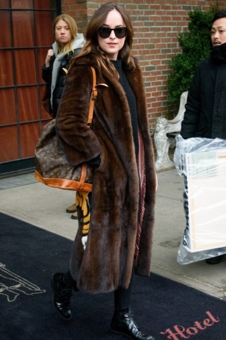 Dakota Johnson w brązowym futrze, czarnym sweterku i z torebką shopper.