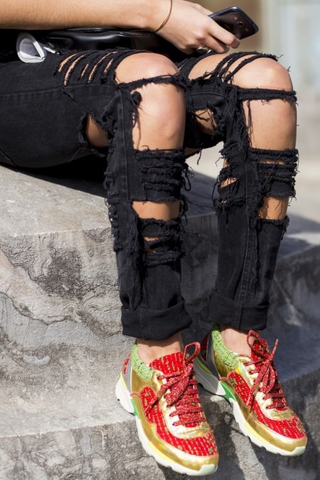 Kolorowe buty sportowe we wzory i czarne jeansy z dziurami.