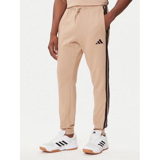 adidas Spodnie dresowe Essentials 3-Stripes JX0712 Beżowy Regular Fit ze sklepu MODIVO w kategorii Spodnie męskie - zdjęcie 184672761