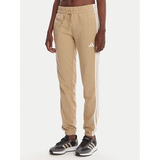adidas Spodnie dresowe Essentials 3-Stripes JX7661 Beżowy Regular Fit ze sklepu MODIVO w kategorii Spodnie damskie - zdjęcie 184722420