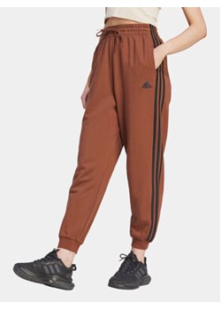 adidas Spodnie dresowe Essentials 3-Stripes IL3451 Brązowy Loose Fit ze sklepu MODIVO w kategorii Spodnie damskie - zdjęcie 168558090