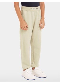 Calvin Klein Jeans Spodnie dresowe Intrasia Logo IB0IB02081 Beżowy Regular Fit ze sklepu MODIVO w kategorii Spodnie chłopięce - zdjęcie 170507632