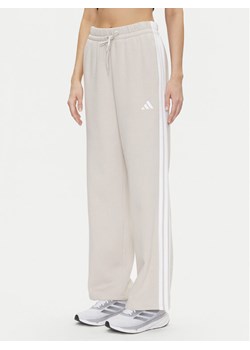 adidas Spodnie dresowe Essentials 3-Stripes JW9215 Beżowy Regular Fit ze sklepu MODIVO w kategorii Spodnie damskie - zdjęcie 182701043