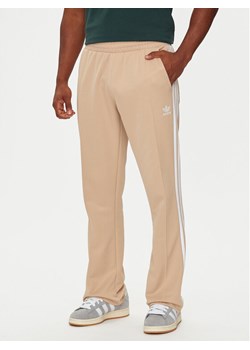 adidas Spodnie dresowe adicolor 70's IX5221 Beżowy Regular Fit ze sklepu MODIVO w kategorii Spodnie męskie - zdjęcie 182726682