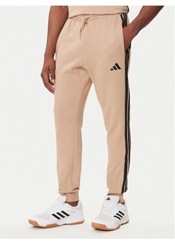adidas Spodnie dresowe Essentials 3-Stripes JX0712 Beżowy Regular Fit ze sklepu MODIVO w kategorii Spodnie męskie - zdjęcie 184672761