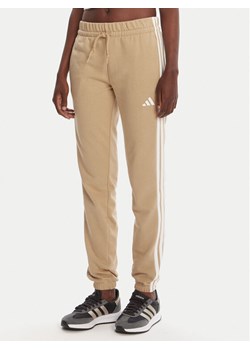adidas Spodnie dresowe Essentials 3-Stripes JX7661 Beżowy Regular Fit ze sklepu MODIVO w kategorii Spodnie damskie - zdjęcie 184722420