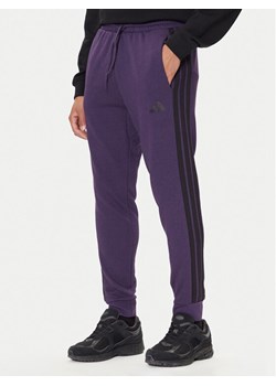 adidas Spodnie dresowe Essentials 3-Stripes JX0750 Fioletowy Regular Fit ze sklepu MODIVO w kategorii Spodnie męskie - zdjęcie 186125183