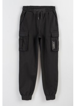 Spodnie materiałowe typu joggery z przestrzennymi kieszeniami, Rozmiar - 140, Kolor - Czarny ze sklepu REPORTER w kategorii Spodnie chłopięce - zdjęcie 189107413