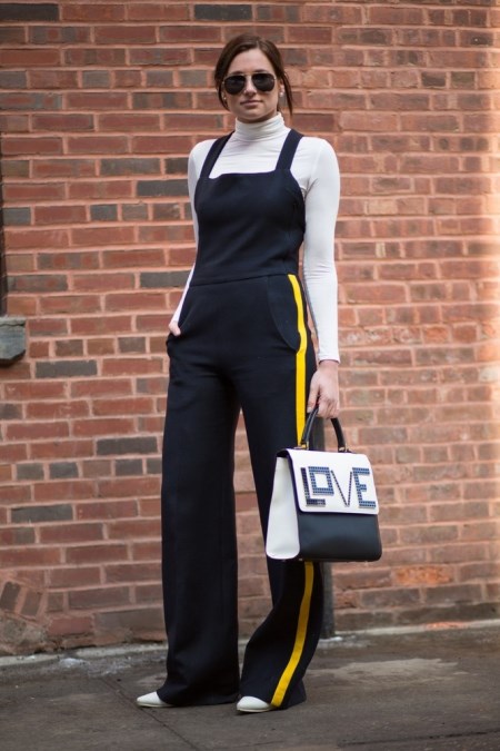 Kobiet ubrna w elegenackie ogrodniczki, kremowy golf i torebkę z napisem "love".