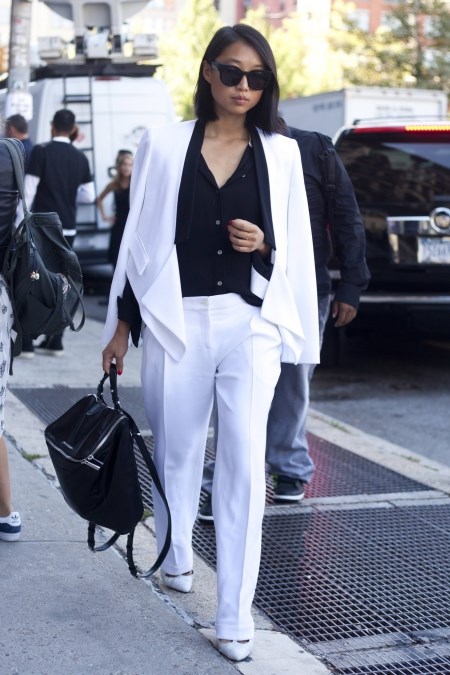 Kobieta w białym garniturze damskim i z eleganckim czarnym plecakiem skórzanym.